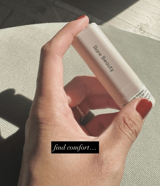Selena Gomez's hand with a burnt orange manicure holding a lip butter lab sample